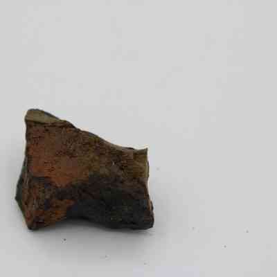 Closeup of basaltic glass core: The image depicts a rough, angular basaltic glass core specimen, displaying various earthy tones, resting against a clean, white background.