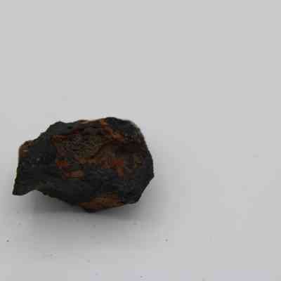 Closeup of basaltic glass core: The image shows a small, rugged basaltic glass core with a dark, textured surface contrasting against the plain background.