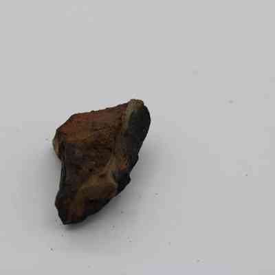 Closeup of basaltic glass core: A basaltic glass core with dark, rough surfaces and a slightly angled shape lies against a plain white background.