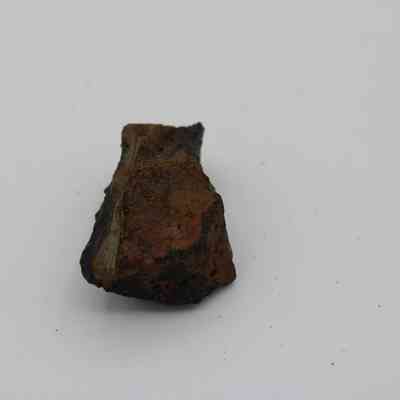 Closeup of basaltic glass core: The image shows a piece of basaltic glass core with rough, uneven textures and visible dark and earthy tones.
