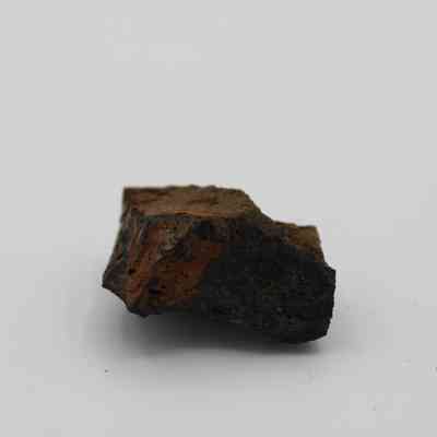 Closeup profile of basaltic glass core: The image shows a rough, dark basaltic glass core with a textured surface, resting against a plain, light background.