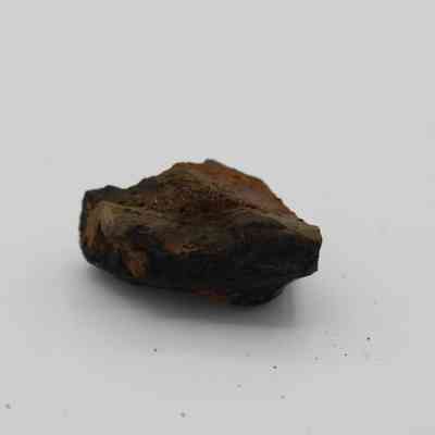 Closeup profile of basaltic glass core: The image shows a rough, dark brown basaltic glass core resting on a stark white surface.