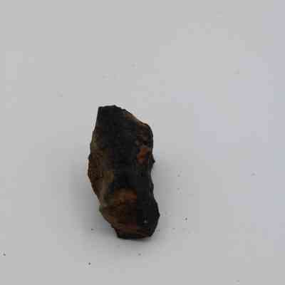Closeup of basaltic glass core: The image shows a black basaltic glass core with a rough, angular texture and brownish-orange patches against a plain background.