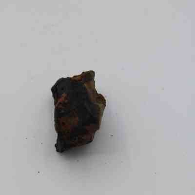 Closeup of basaltic glass core: The image shows a small piece of basaltic glass core, dark and rugged, placed prominently on a plain, light-colored background.