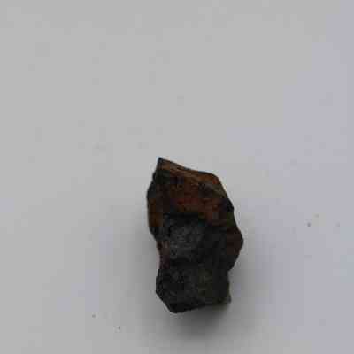 Closeup of basaltic glass core: The image shows a small, rough piece of basaltic glass core, displaying dark and earthy colors against a plain background.
