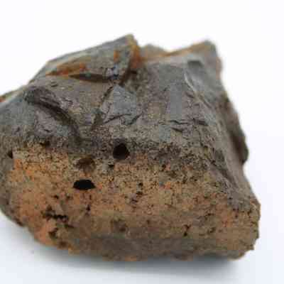 Closeup of side profile of basaltic glass core: The image shows a weathered basaltic glass core with a rough, porous texture, featuring dark and rusty brown hues throughout.