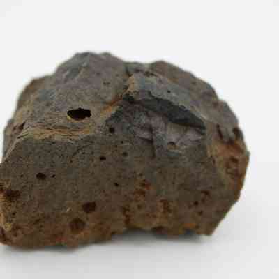 Closeup of basaltic glass core: The image displays a rough-textured basaltic glass core, with small cavities and a dark, uneven surface.