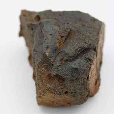 Closeup of basaltic glass core: The image shows a jagged piece of basaltic glass with smooth, dark surfaces and rough, irregular edges resting against a plain background.