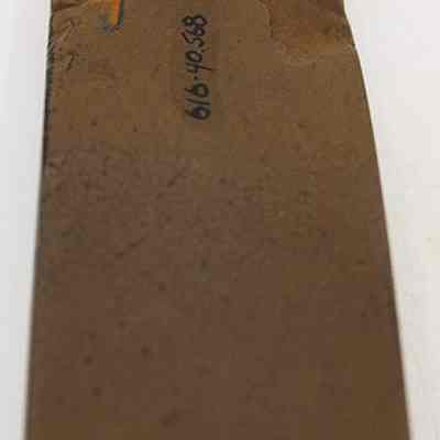 Lengthwise view of polished side of basalt adze (ko'i) fragment: The image shows an ancient adze (ko'i) fragment with a roughly rectangular shape and a dark surface, marked with numbers for cataloging purposes.