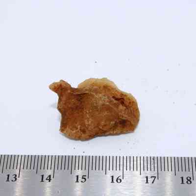Closeup of calcite piece with ruler: A small, irregularly shaped calcite stone lies beside a ruler on a white background, highlighting its size and texture.