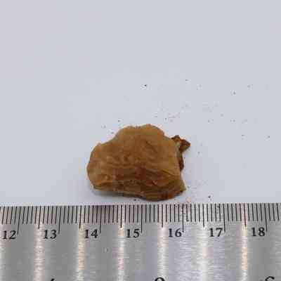 Closeup of calcite with ruler: A small, brown calcite mineral sample is placed on a flat surface next to a ruler for size reference, showing fine, layered textures.