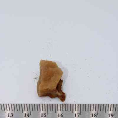 Tight closeup of a piece of calcite: A small piece of calcite rests on a white surface, accompanied by a ruler for size comparison, highlighting its texture and structure.