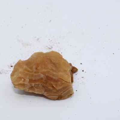 Closeup of a piece of calcite: The image shows a piece of calcite with visible striations, lying on a white surface sprinkled with small dust particles around it.