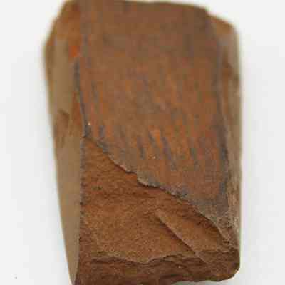 Lengthwise view of basalt adze fragment: The image shows a brown, weathered fragment of an adze, featuring rough edges and a wedge shape, indicative of its utility.