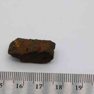 A basaltic glass, pāhoehoe core with a metal ruler: The image shows a small, rough, brownish rock resembling pāhoehoe  lava, placed beside a ruler for scale.