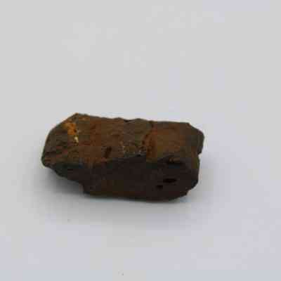 Close up of a basaltic glass, pāhoehoe core: The image shows a small, rough piece of pāhoehoe lava rock with a rugged, dark brown surface and subtle texture.