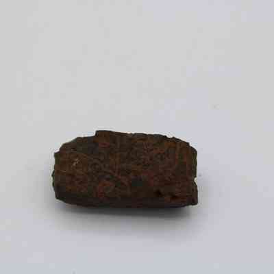 Closeup of basaltic glass, pāhoehoe core: The image depicts a small, dark, textured piece of pāhoehoe lava on a plain white background, showcasing its rough, natural surface.