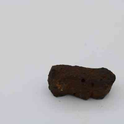 Closeup of basaltic glass, pāhoehoe core: The image shows a small piece of pāhoehoe lava rock, characterized by its smooth, ropy texture, against a plain white background.