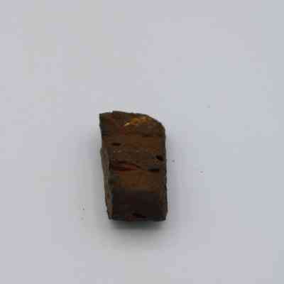 Closeup of basaltic glass pāhoehoe core: The image shows a solitary piece of basaltic glass pāhoehoe, brownish in color, lying on a plain white surface, highlighting its rough texture.