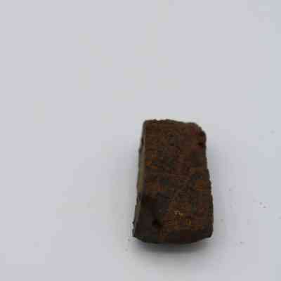 Closeup of basaltic glass, pāhoehoe core: The image shows a rough and textured piece of pāhoehoe lava rock with a reddish-brown hue against a plain white background.