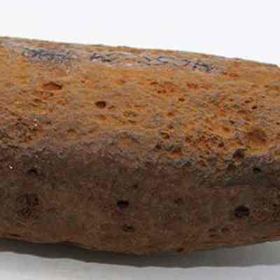 Profile of an adze preform: The image shows a rusty, irregularly shaped rock with a rough, pitted surface, resting on a plain white background.