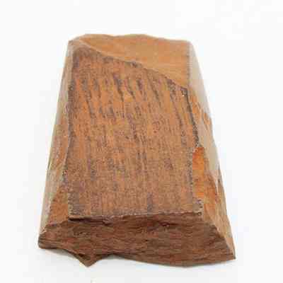 Polished side of basat adze fragment: The image shows a brown stone adze (ko'i) fragment with a smooth, polished surface and visible grain patterns.