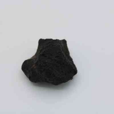 Closeup of basaltic glass core: In the image, a basaltic glass core appears dark and textured, resting alone against a plain light background.