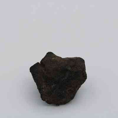 Close up of basaltic glass core: The image shows a dark piece of basaltic glass core with an irregular shape, resting on a plain white background.