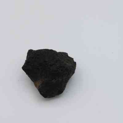 Basaltic glass core: The image shows a rough, dark basaltic glass core lying on a plain white surface, highlighting its irregular texture and shape.