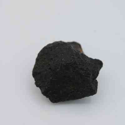 Basaltic glass core: The image shows a dark, rough-textured basaltic glass core against a plain white background, highlighting its volcanic origin.