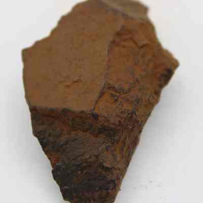 Tip of adze (ko'i) flake: The image shows a brown adze (ko'i) flake with a rough, uneven surface, featuring sharp edges and a weathered appearance, indicative of its archaeological significance.