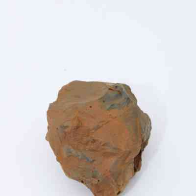 Closeup of basaltic glass core: The image shows a piece of basaltic glass core, exhibiting rough, angular surfaces and brownish-green hues, resting against a plain white background.