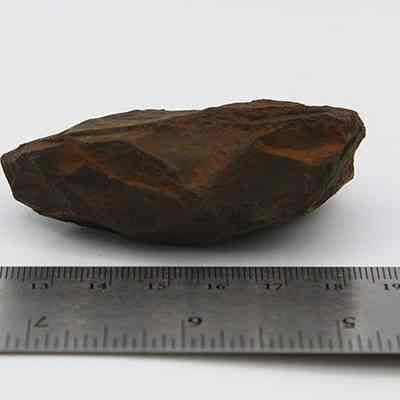 Close up of reverse side of adze preform: The image shows a roughly hewn stone adze preform beside a ruler, indicating its size is approximately 6 cm long.