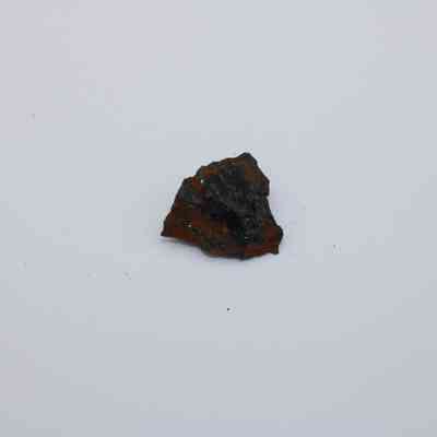 Closeup of basaltic glass core: The image shows a small piece of basaltic glass core with dark and reddish-brown hues, set against a plain white background.