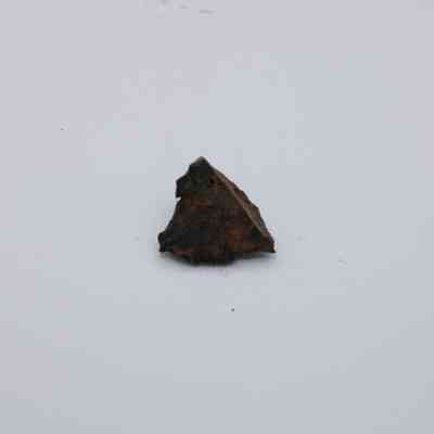 Basaltic glass core closeup: A piece of dark basaltic glass core lies on a plain white surface, highlighting its rugged texture and irregular shape.