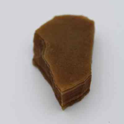 Agate flake: The image shows a brown, translucent agate flake with layered edges, placed against a plain white background, highlighting its natural texture and form.