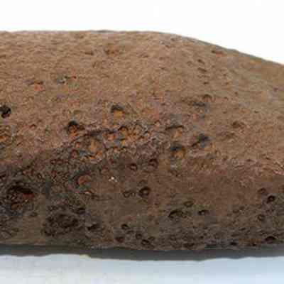 Profile of adze preform: The image shows a rough-textured, brownish rock with a slightly elongated shape, lying horizontally against a plain white background.