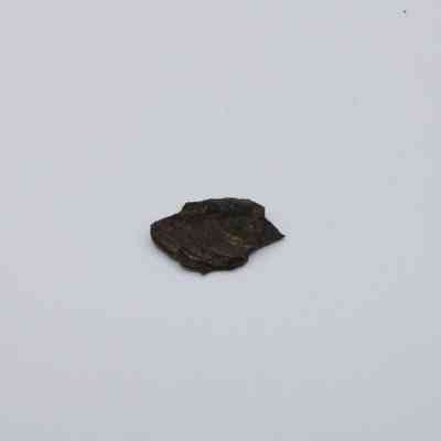 Closeup of tiny basaltic glass flake: The image shows a small, dark basaltic glass flake resting on a plain white background, highlighting its textured, volcanic origin.