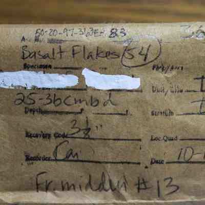 Sample paper bag for basalt blakes: The image shows a labeled brown paper bag with handwritten details about basalt flakes, location coordinates, and excavation information dated 10-14-83.