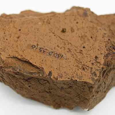 Grinding stone with alternate id number visible: The image shows a rough, brown grinding stone with a labeled number inscribed on its surface, set against a plain white background.