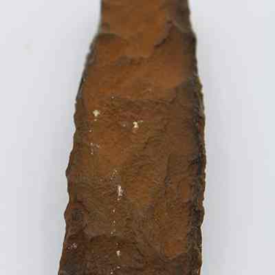 Lengthwise view of quadrangular adze: The image shows a close-up of a brown, rough-textured, rectangular stone tool on a plain white background.
