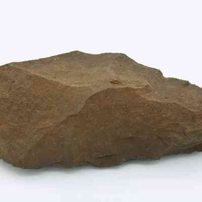 Top of adze blank: The image shows a rough, unfinished stone adze blank with a pointed end, lying against a plain white background.