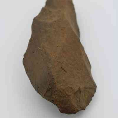 Lengthwise view of adze blank and ruler: The image shows a roughly hewn, brown stone adze blank beside a ruler measuring its size in centimeters.