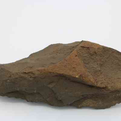 Adze blank profile: The image shows a roughly-shaped, brown stone adze blank, with uneven surfaces and sharp edges, typical of a prehistoric tool in its early stage.