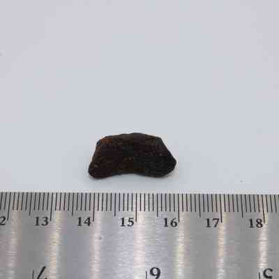 Small basaltic glass core and ruler: The image shows a small piece of basaltic glass core placed next to a metal ruler with centimeter markings on a white surface.