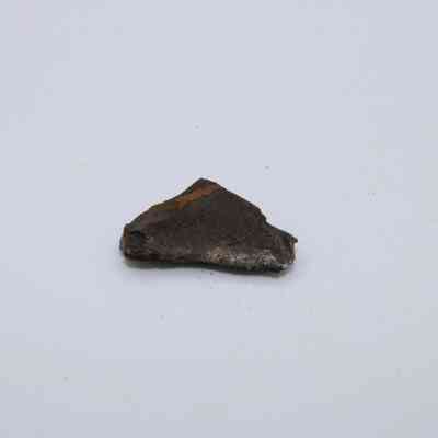 Basaltic glass flake: A small piece of basaltic glass flake rests on a light surface, showcasing its dark, glassy texture with subtle reflections.