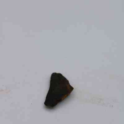 Basaltic glass flake: A small, dark basaltic glass flake lies against a plain white background, showing its rugged texture and irregular shape in the center.