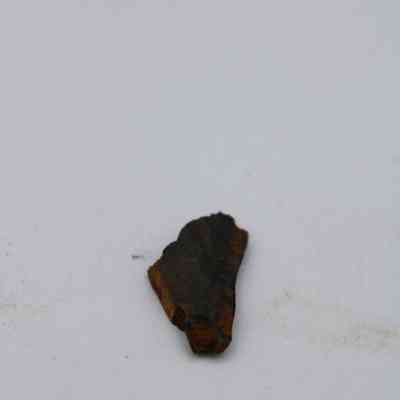 Closeup of basaltic glass flake: The image shows a small, irregular basaltic glass flake on a plain, light-colored surface.