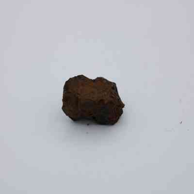 Closeup of small core of basaltic glass: The image shows a small, irregularly-shaped basaltic glass core resting against a plain gray background.