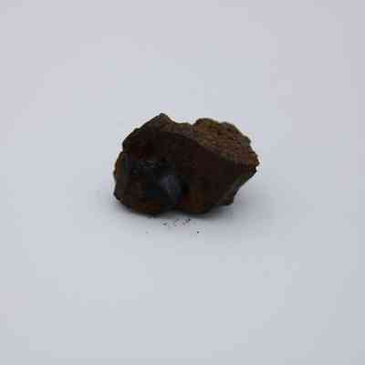 Closeup of basaltic glass core: The image features a small piece of basaltic glass core, showcasing its rough, dark surface against a plain, light background.